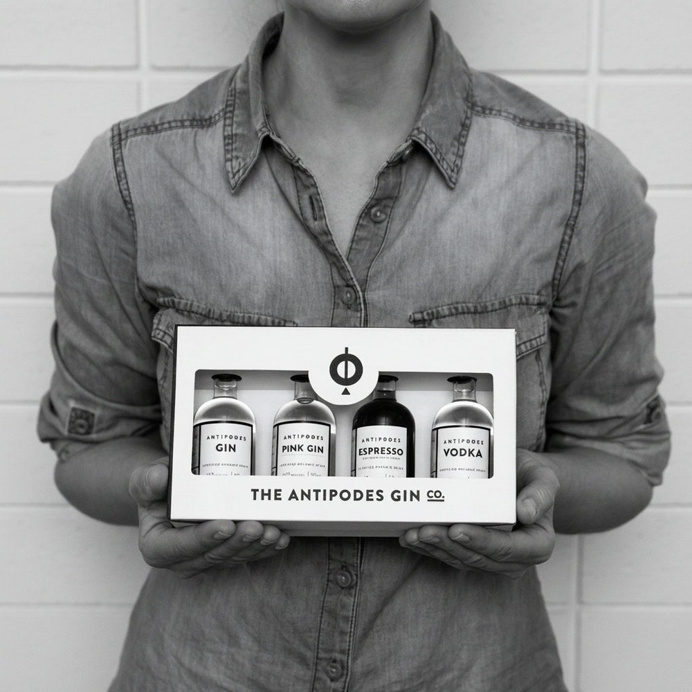 Person holding a box of The Antipodes Gin Co. products against a white brick wall.