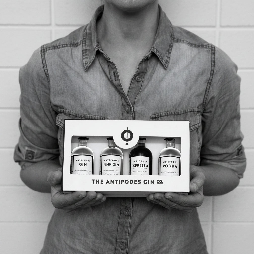 Person holding a box of The Antipodes Gin Co. products against a white brick wall.