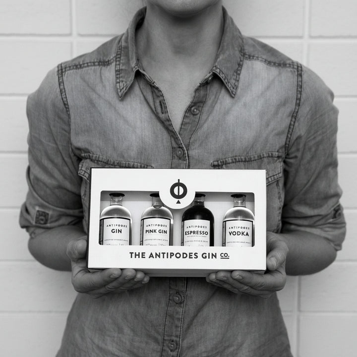 Person holding a box of The Antipodes Gin Co. products against a white brick wall.