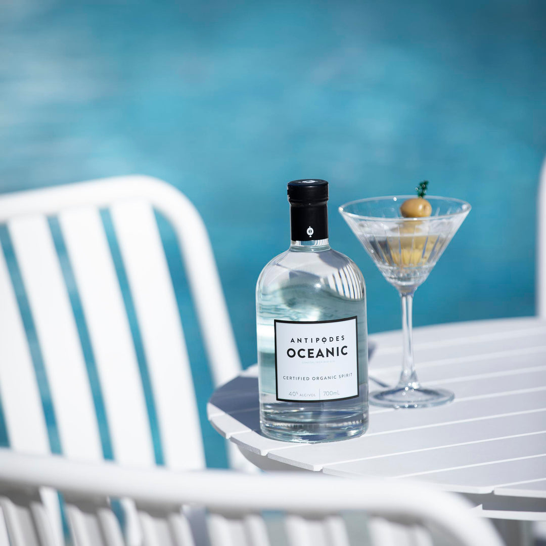 Bottle of Antipodes Oceanic gin with a cocktail glass on a white table outdoors.