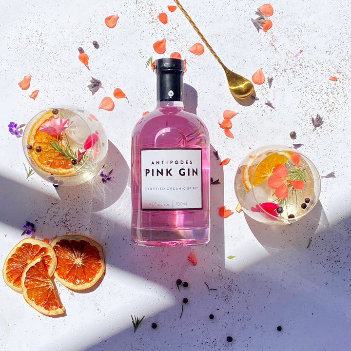 Pink gin bottle with floral and fruit garnishes on a light background