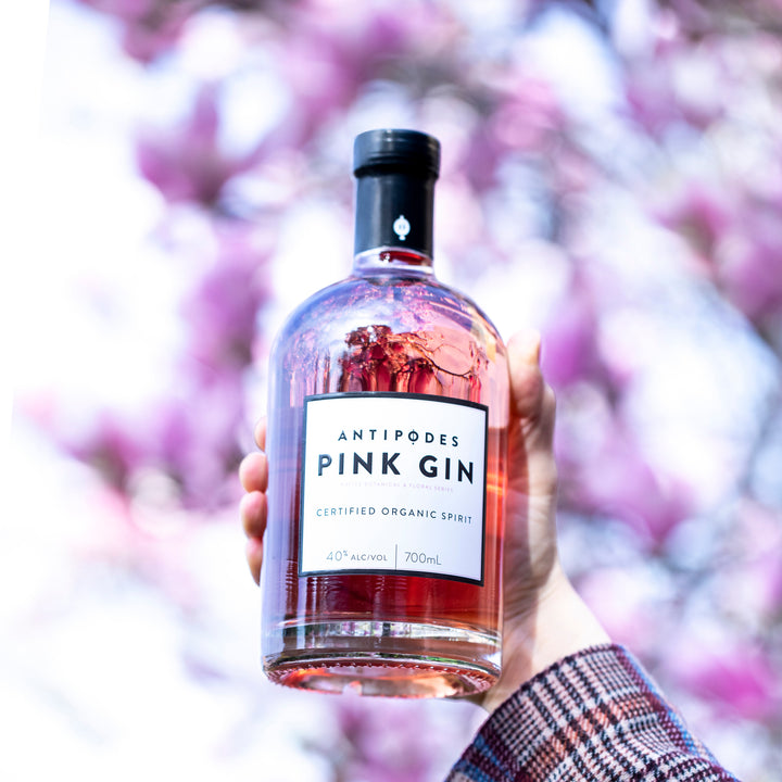 Bottle of Antipodes Pink Gin held in front of a blurred purple floral background