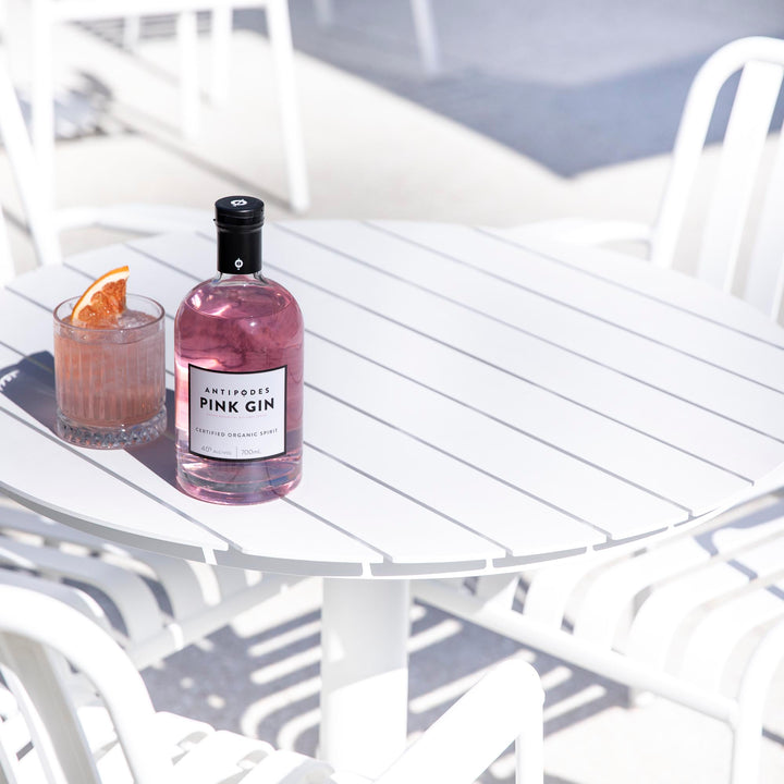 Bottle of pink gin and a glass with a slice of orange on a white table outdoors.