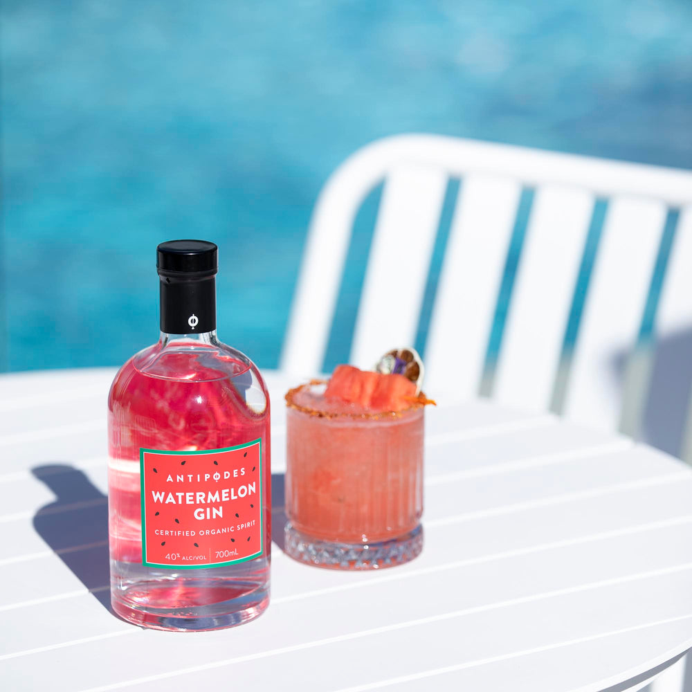 Bottle of Antipodes Watermelon Gin with a glass of pink cocktail on a white chair by a pool.